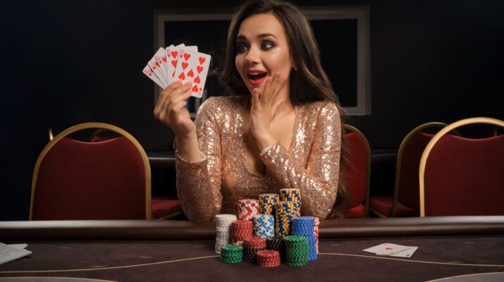 happy brunette girl brilliant gold dress is playing poker sitting table casino she is making bets waiting big win showing her cards gambling money games fortune